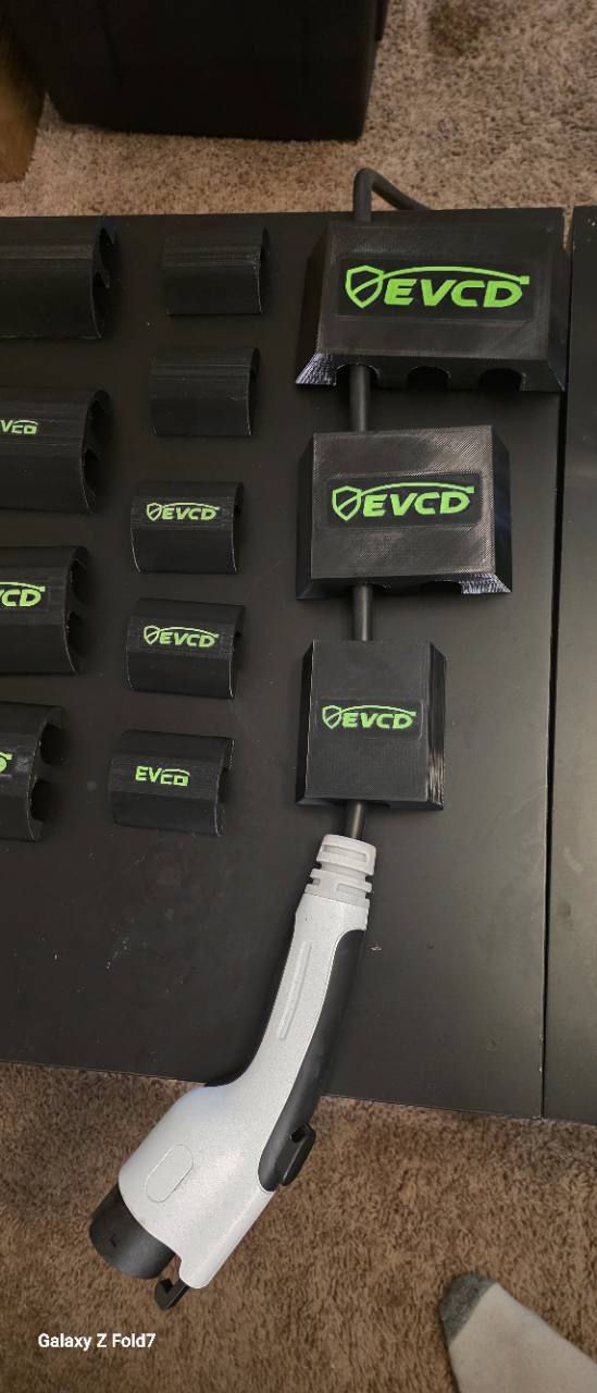 EV charger connector and black charging cable arranged with EVCD Solo, Duo, and Trio guards on a workbench