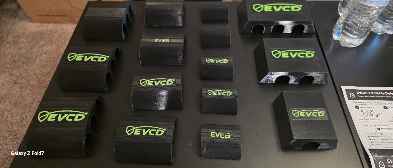 Full EVCD family of black PETG cable guards with green logos arranged on a workbench